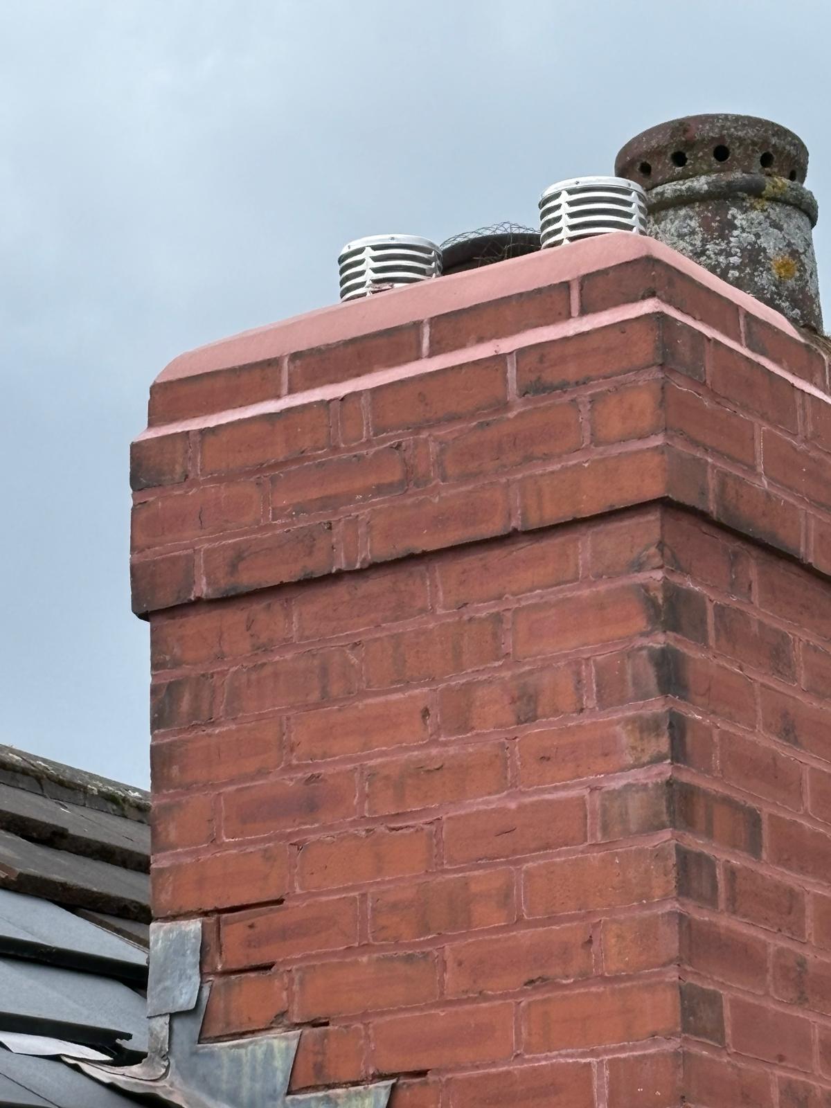 A rebuilt chimney stack with fresh mortar against grey tiles